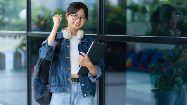 Mahasiswi membawa laptop dan tas, mengenakan headphone di leher
